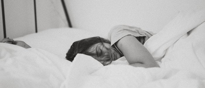 Woman with messy hair is sleeping in a white bed with messy sheets. Showing how to get better sleep.